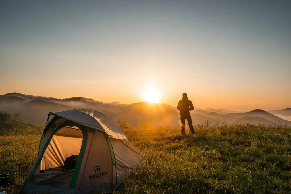 Person vor Zelt beim Camping in den Bergen Süddeutschlands bei Sonnenuntergang