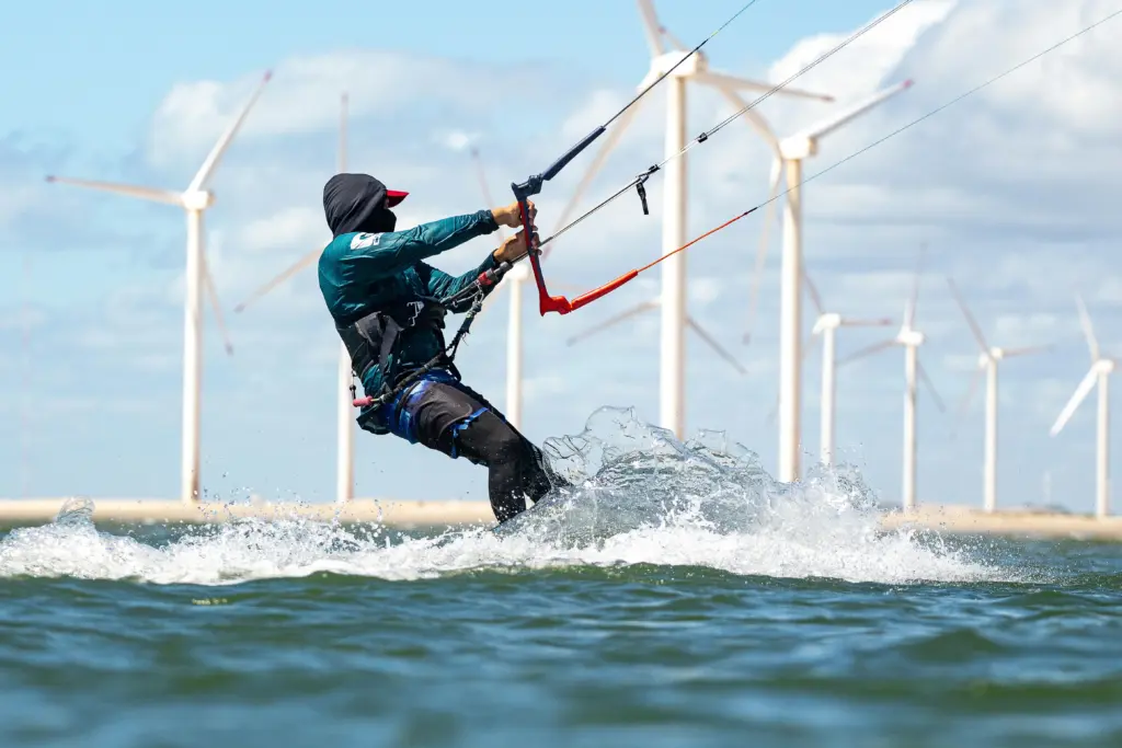 Surfer beim Kitesurfen im Meer mit Windrädern im Hintergrund – sportliches Highlight beim Sommercamping am Wasser.