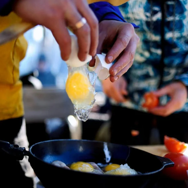 Camping Rezepte: Ei wird über der Pfanne geöffnet – frische Zutaten beim Kochen draußen