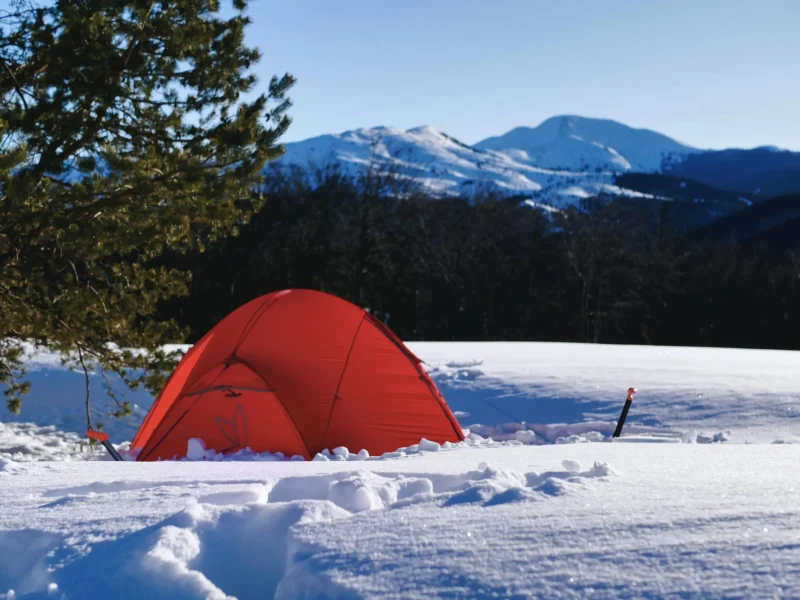 Wintercamping im Schnee mit rotem Zelt in verschneiter Landschaft