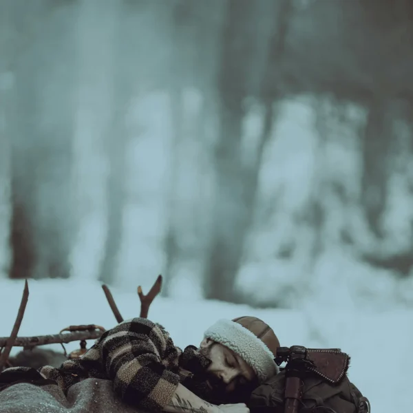 Wintercamping: Mann schläft im Schnee unter einer Decke in winterlicher Landschaft