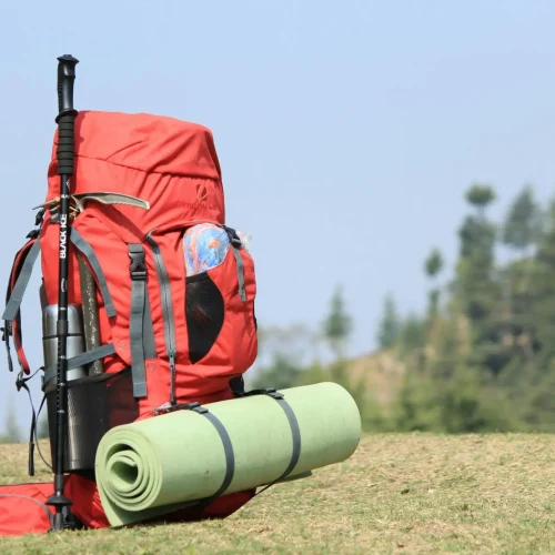 Wildcamping-Ausrüstung – Rucksack mit Isomatte im Gelände Wildcamping: Roter Rucksack mit befestigter Isomatte für Outdoor-Abenteuer