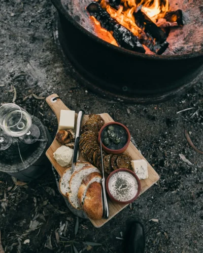 Wintercamping: Warme Mahlzeit am Lagerfeuer Wintercamping: Essen auf Holzbrett neben Lagerfeuer in der winterlichen Natur